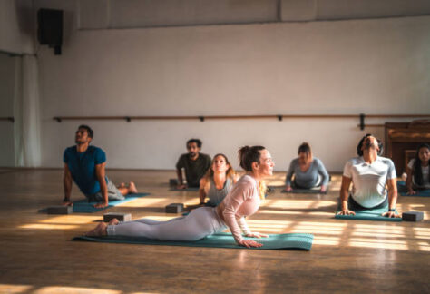 An international group of sporty people doing pilates on the mats in a quiet fitness gym, strong morning light coming from the windows. Full length image.